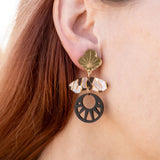 Close-up of a person with long auburn hair wearing handcrafted Kintsugi Earrings featuring a gold leaf, a clear crystal, and a black circular charm with a cut-out sunburst design inspired by Japanese art.