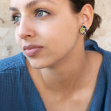 A young woman with light eyes and brown hair pulled back, wearing a textured blue top and lightweight Minimalist Geometric Stud Earrings, looks thoughtfully to the side against a beige, textured wall.