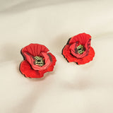 A pair of red, poppy design acrylic earrings with black and green centers, displayed on a soft, light-colored fabric background. Lightweight and eye-catching for any occasion.