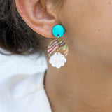 Close-up of a woman’s ear wearing a handmade, colorful earring with a turquoise stud, wavy striped section, and white floral-shaped dangle. Her hair is pulled back and she is wearing a white top. Lightweight for all-day comfort.